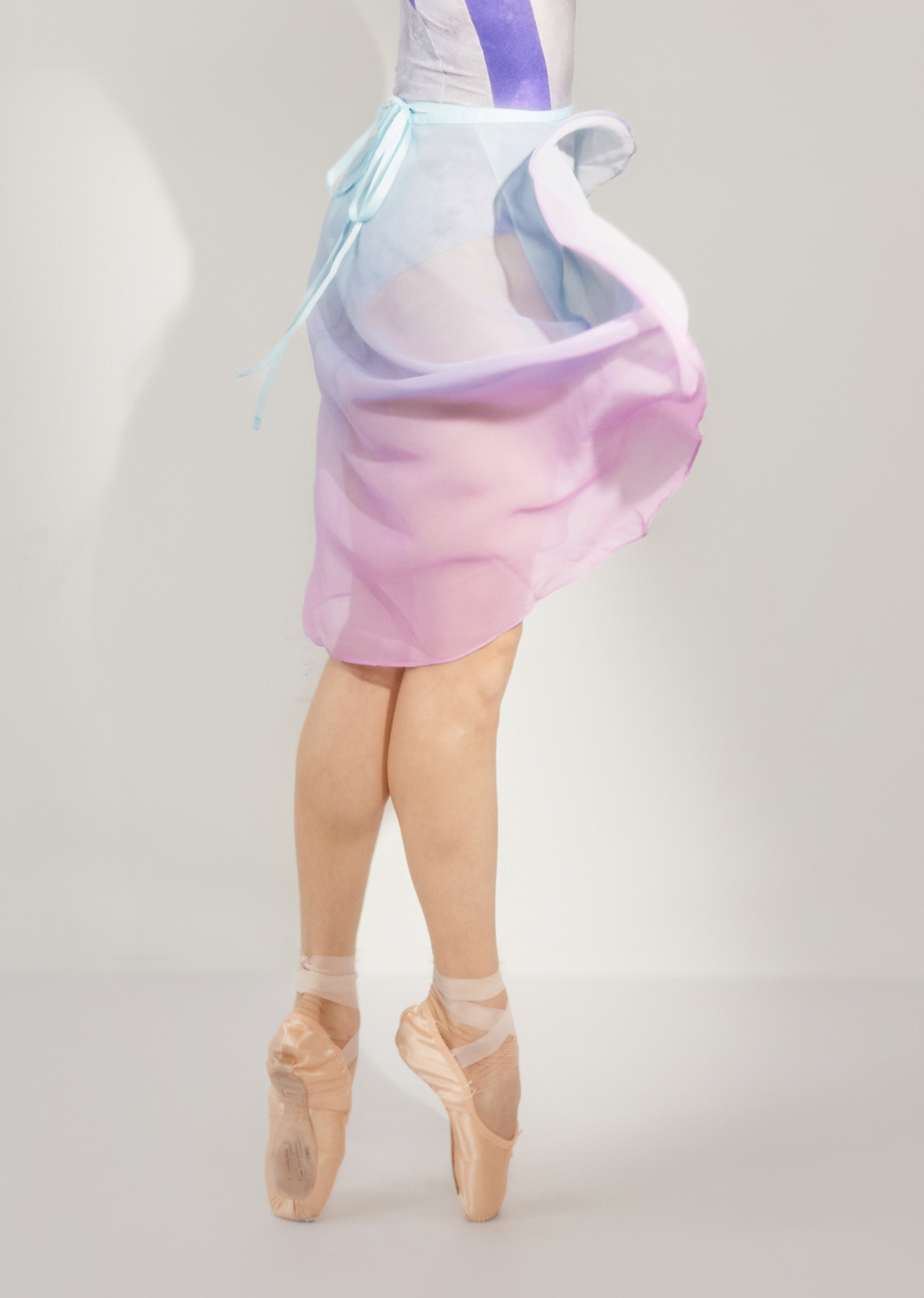 A ballet dancer wearing a long ombré ballet skirt in shades of purple and blue, with a grosgrain ribbon, floating in the air.