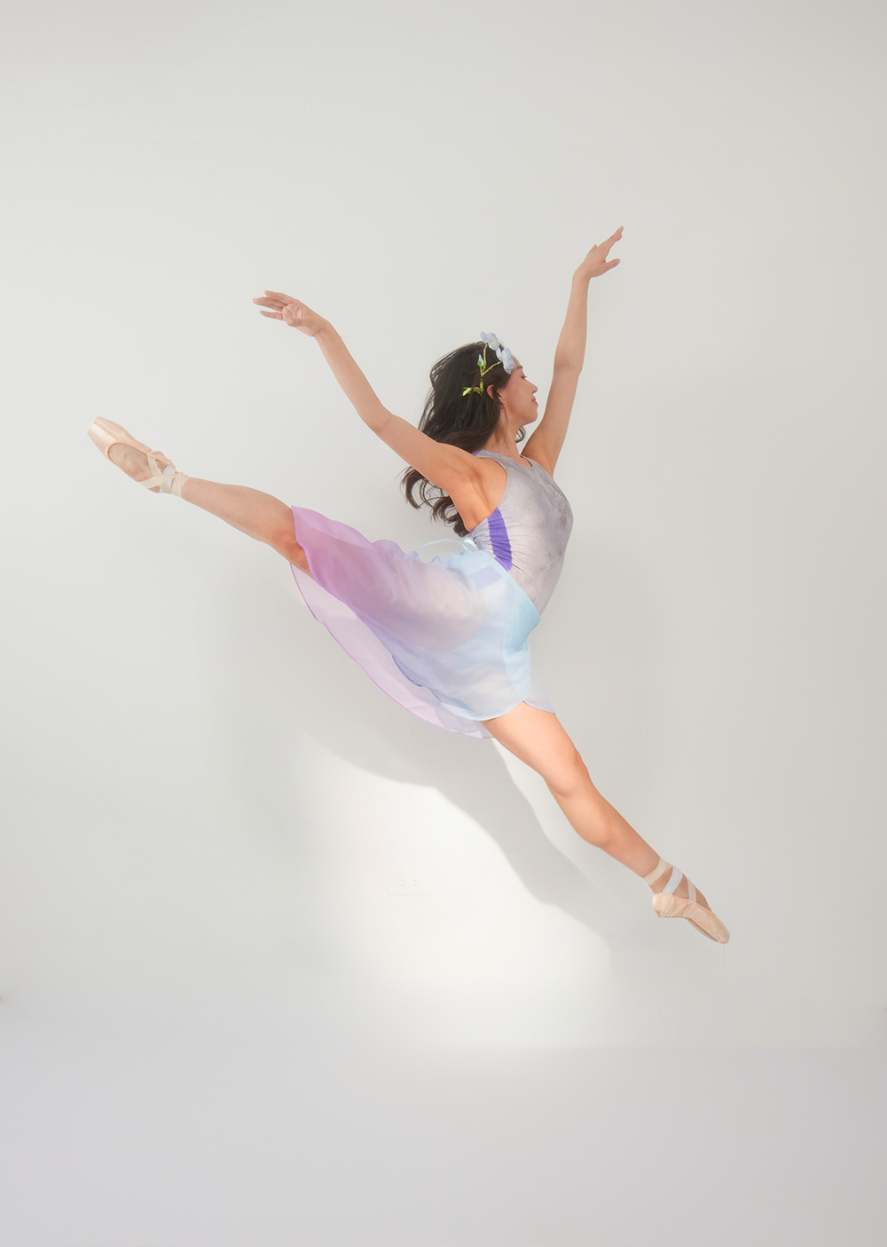 Dancer in a colorful dress performing a jump against a plain background