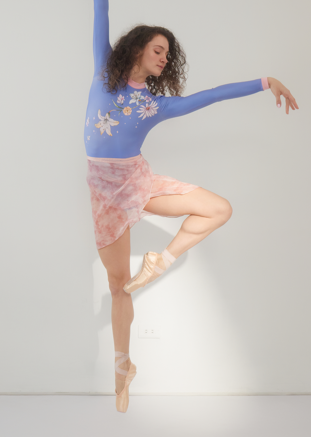 Dancer in a blue floral top and pink skirt on a gray background